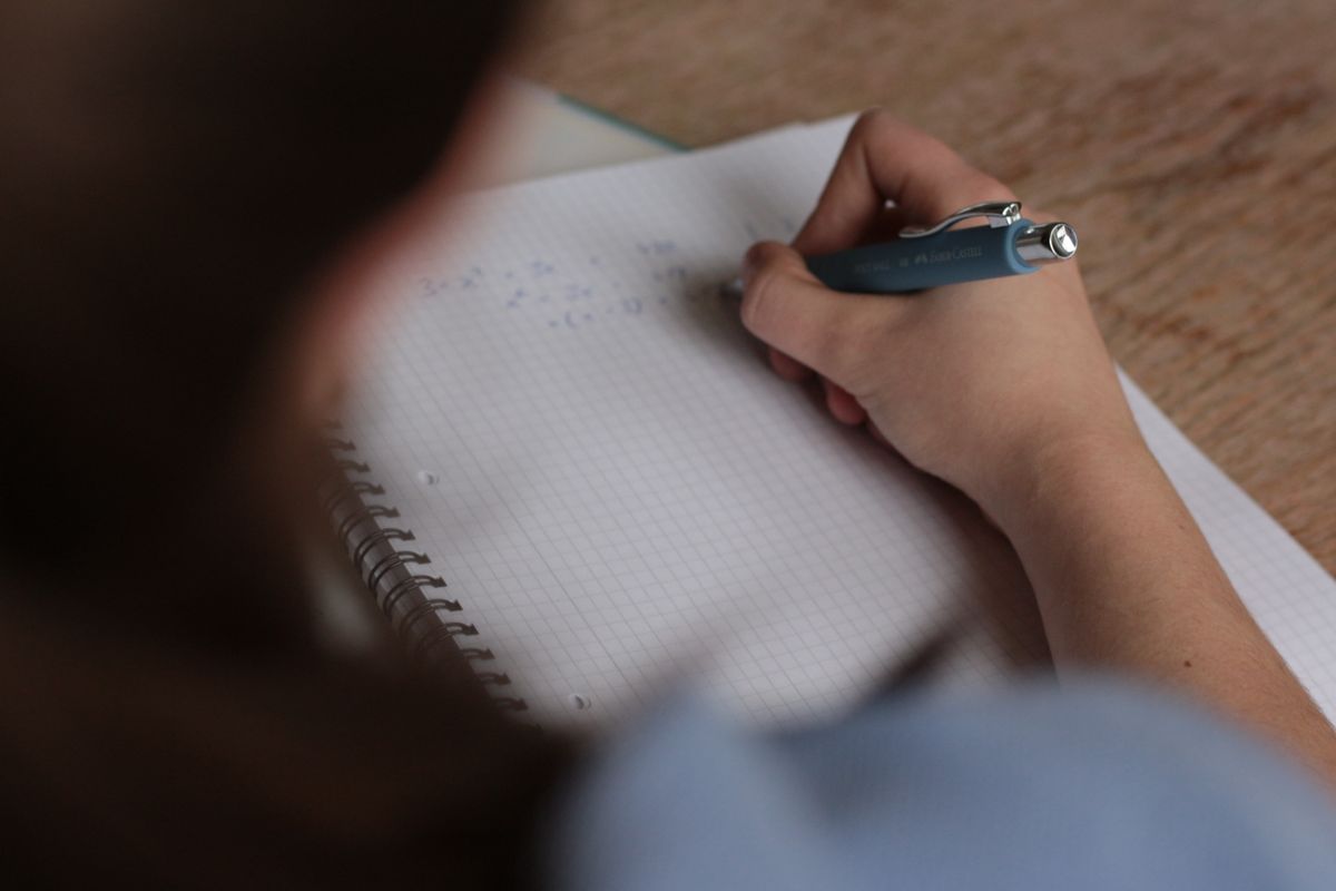 Élève qui écrit des formules de maths dans un cahier à carreaux